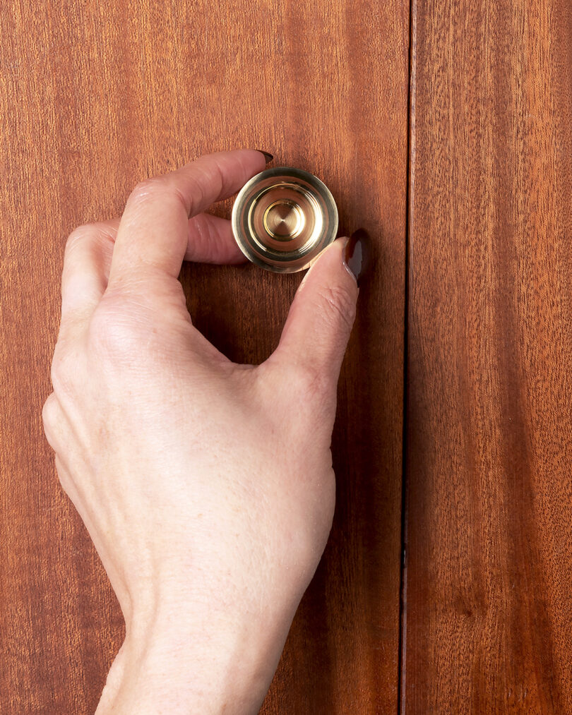 A hand is grasping a brass knob on a wooden cabinet door