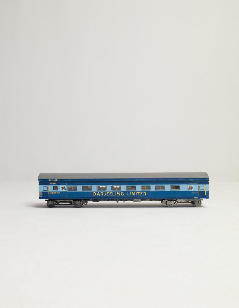 A model train car painted blue with "Darjeeling Limited" written on the side, positioned against a plain, light background.