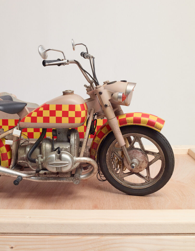A vintage motorcycle with red and yellow checkerboard patterns displayed on a light wooden platform.